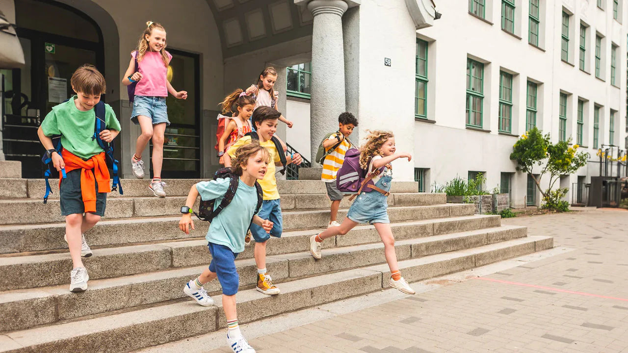 Lapset juoksevat ulos koulurakennuksesta reppujen kanssa – iloinen hetki koulupäivän päätyttyä
